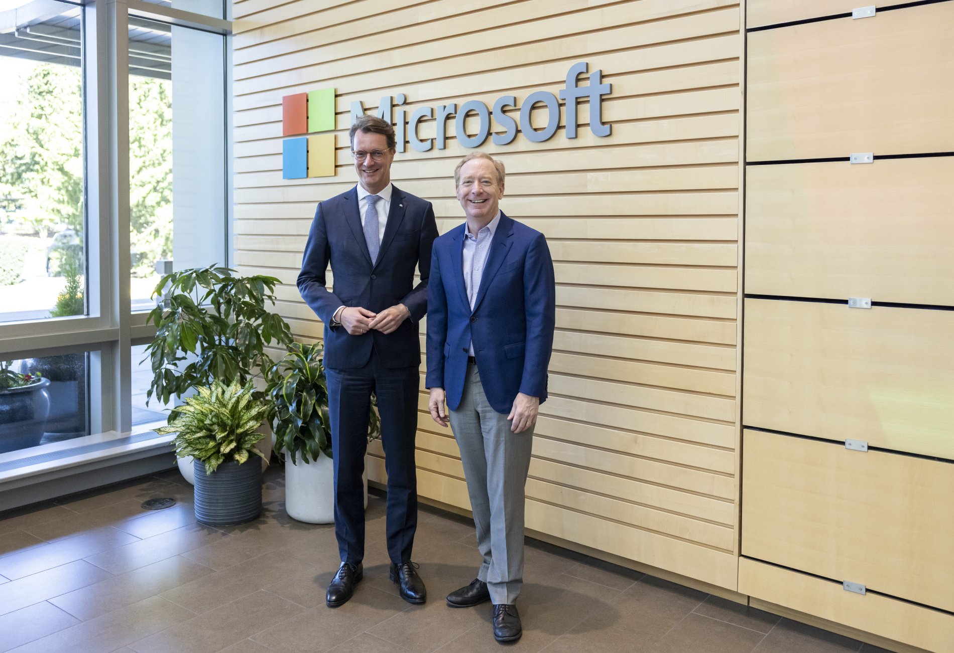 Der Ministerpräsident Hendrick Wüst und Vice-Chair und President von Microsoft Brad Smith vor dem Microsoft-Logo